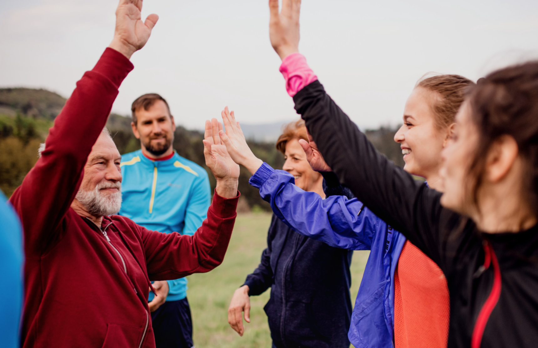 Group of people outdoors giving each other high-fives, smiling and celebrating together.