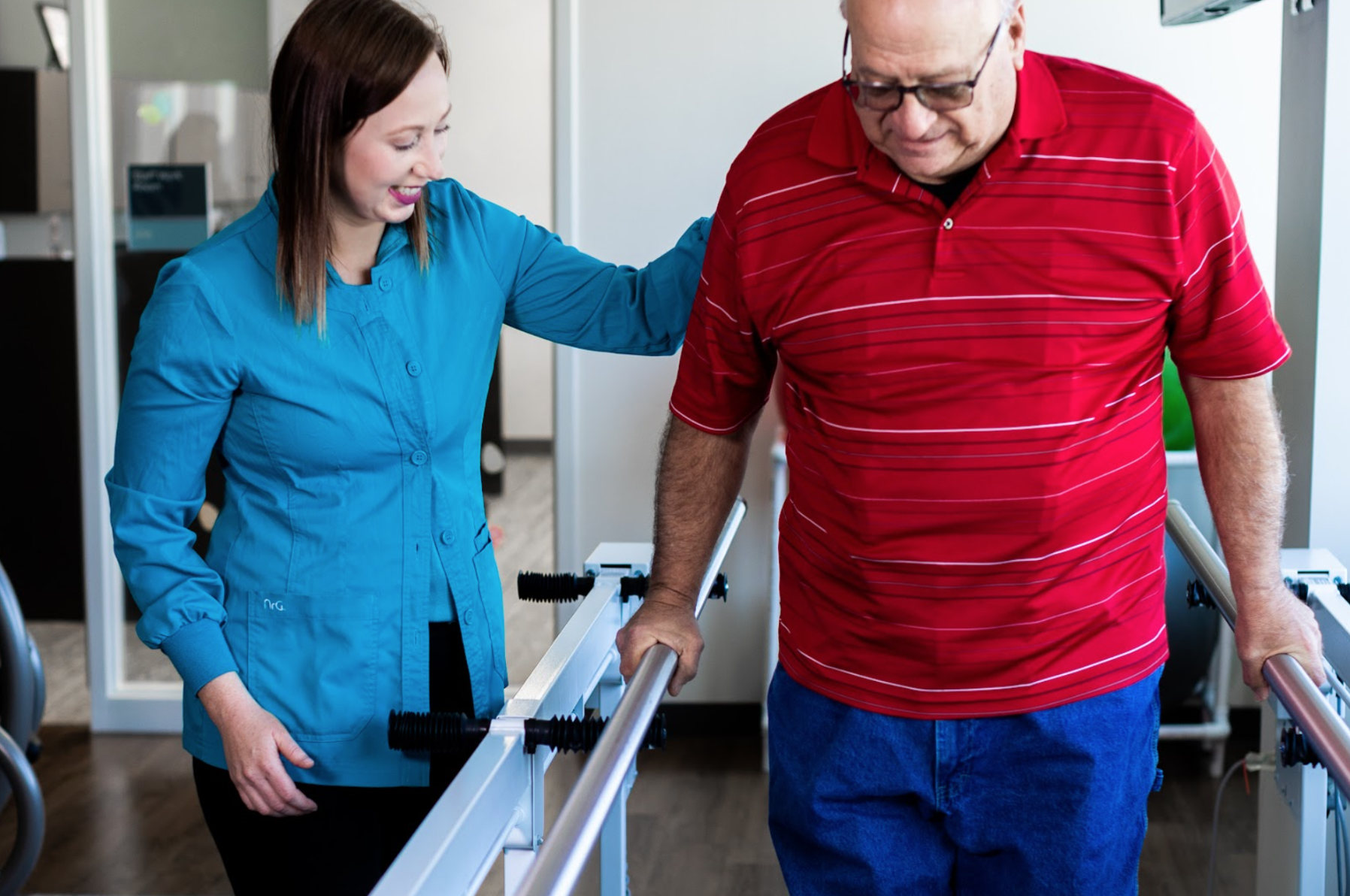 Physical therapist assisting an older man during a rehabilitation exercise with parallel bars.