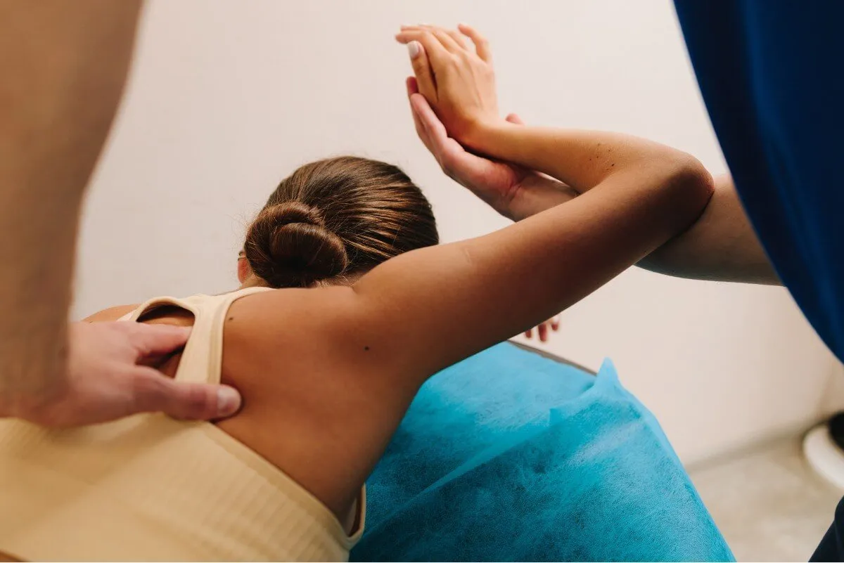 Physical therapist assisting a woman with a shoulder stretch while she lies on a treatment table.