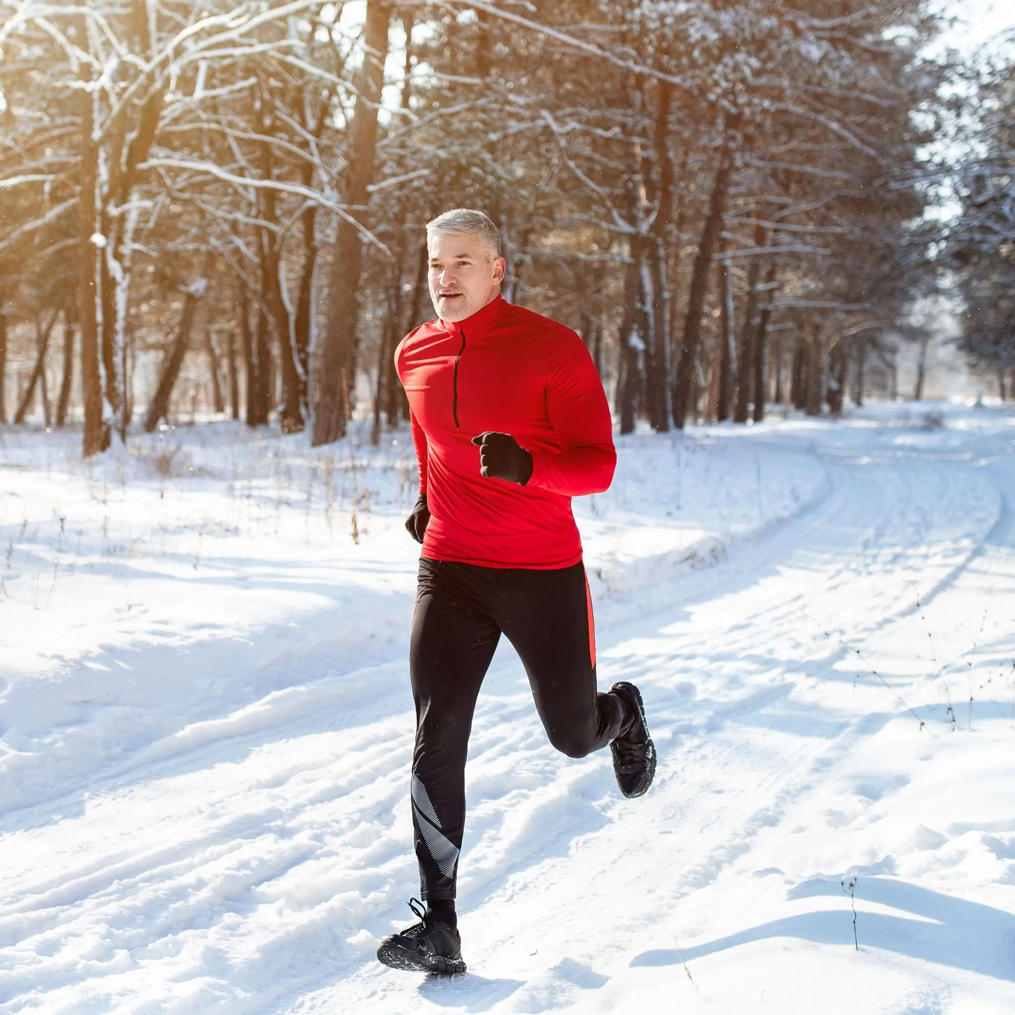 Man jogging through a snowy forest trail in winter, wearing a bright red jacket and black running gear.
